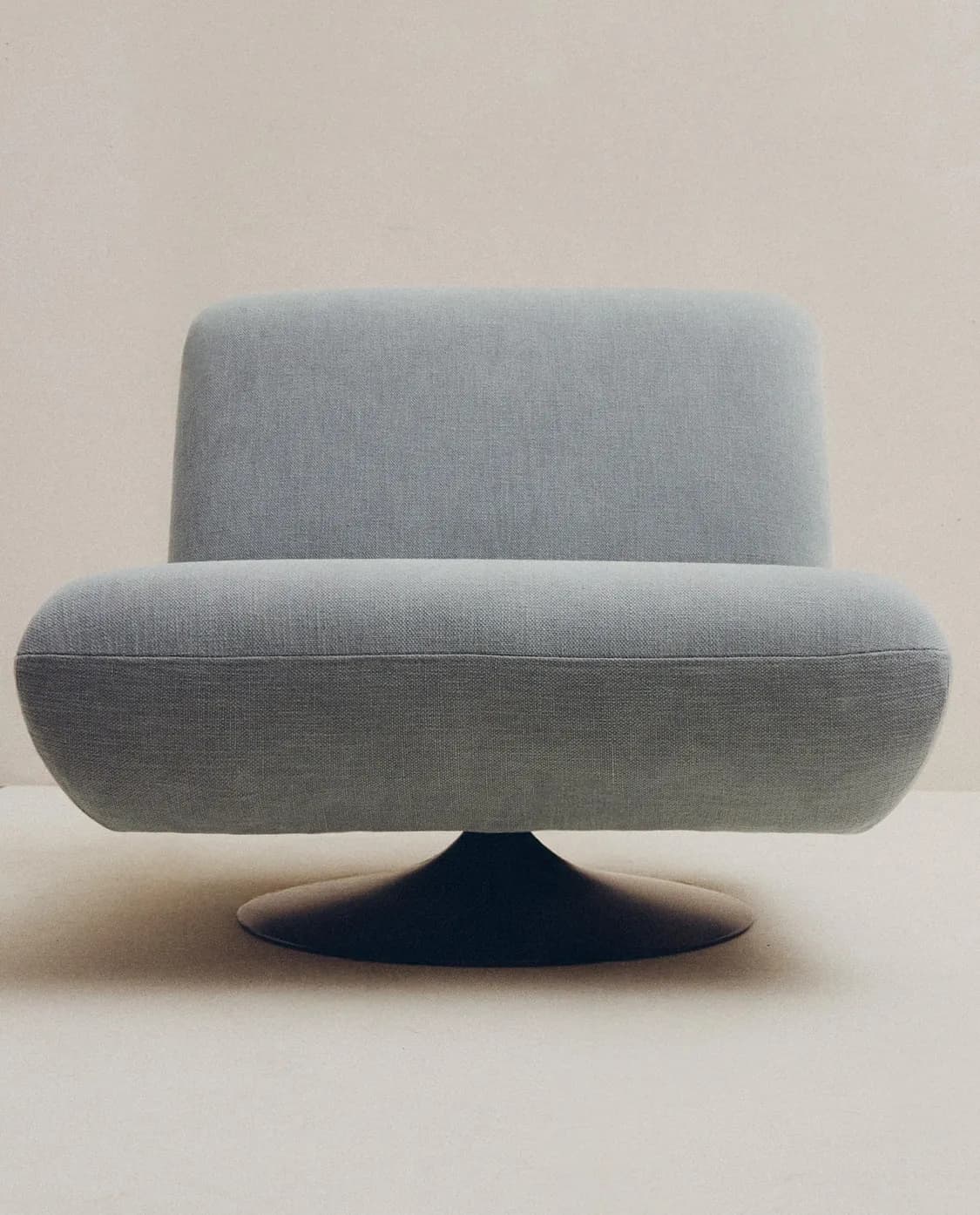 A contemporary swivel lounge chair with a low profile and rounded, organic forms. It features light bluish-grey textured fabric upholstery and sits on a dark, conical swivel base, suggesting modern design and comfort. — 3D model