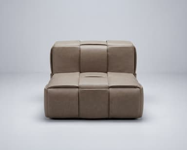 A modular armchair with a low profile and cushioned seating. The piece is characterized by its woven or quilted exterior, creating a series of padded segments. It appears to be upholstered in a soft material, possibly leather or a high-quality faux leather. The design is contemporary and minimalist, with clean lines and a focus on comfort and texture. — 3D model
