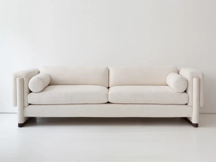 A modern, upholstered sofa with a rectangular frame and distinct cylindrical armrests. The sofa features a two-cushion seat and a three-pillow back, including two standard rectangular back cushions and two cylindrical bolster pillows placed at the ends. The base is a dark, rectangular plinth. The upholstery has a textured weave. — 3D model