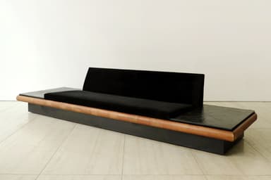 A long, low, contemporary sofa featuring a black velvet upholstered seat and a gently curved backrest, flanked by integrated dark, textured stone side tables, all set within a dark rectangular base with a continuous rounded wooden trim. — 3D model