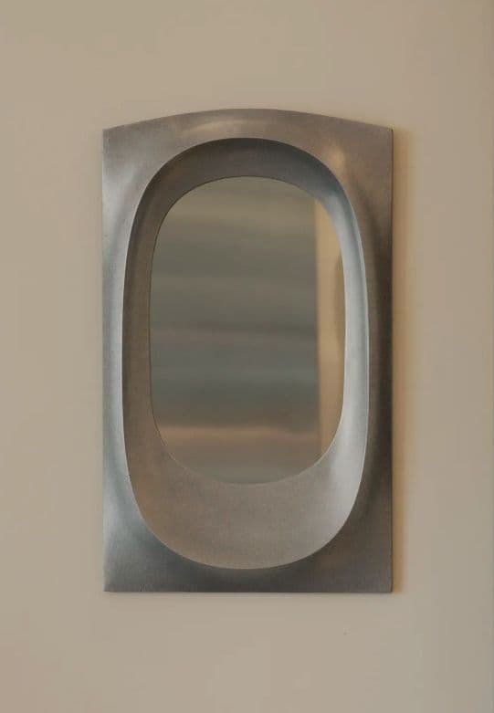 A rectangular wall mirror featuring a deep, organically shaped recessed opening for the reflective surface. The frame appears to be made of a substantial cast metal with a matte gray finish. — 3D model