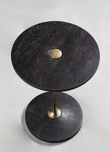 A circular side table with a dark-colored top and base, connected by a slender brass-colored stem. The top surface features a subtle, oval-shaped inlay of a lighter material, possibly brass or a similar metal, positioned centrally. The base is a flat, wide circle, providing stability. — 3D model