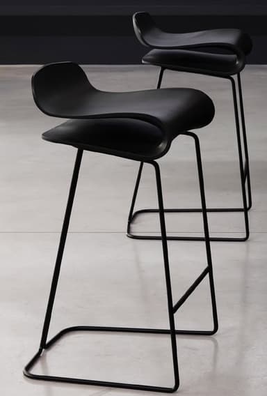 A modern black bar stool with a distinctive, flowing seat that curves upwards at the edges. The seat appears to be a single molded piece. The stool has a slim, black metal frame with four legs connected by a crossbar near the bottom for stability. The legs are angled outwards. — 3D model