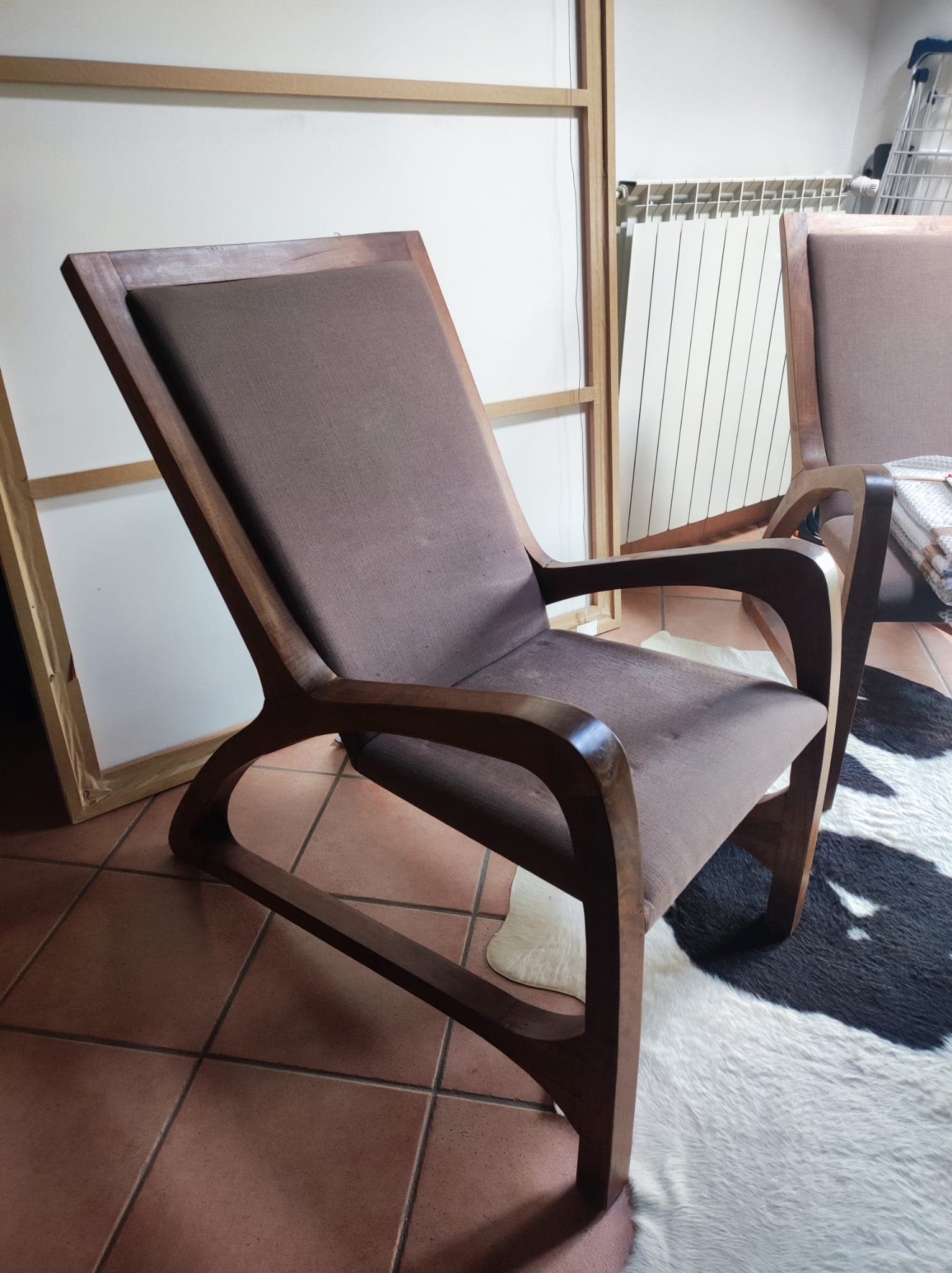 A modern lounge chair featuring a dark-stained solid wood frame with elegantly curved armrests and base. The backrest is angled for comfort, and both the seat and back are upholstered in a neutral taupe fabric. — 3D model