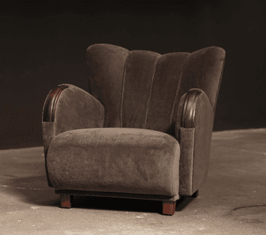 A robust, fully upholstered armchair viewed from the rear-right side, featuring a rounded backrest, integrated arms, and short, dark wooden legs. The chair is covered in a soft, dark taupe fabric. — 3D model