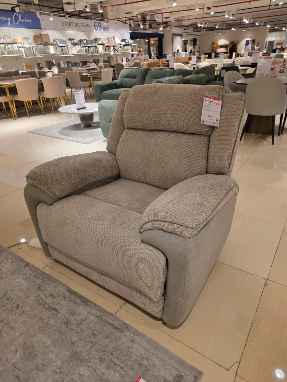 A contemporary upholstered recliner chair featuring a two-tone fabric design. The main body is covered in a light beige, textured fabric, while the lower frame and parts of the armrests are accented with a slightly darker, plain beige or light brown fabric. The chair has plush, padded cushioning on the seat, backrest, and armrests, indicating comfort and support. It appears to be in excellent, new condition. — 3D model
