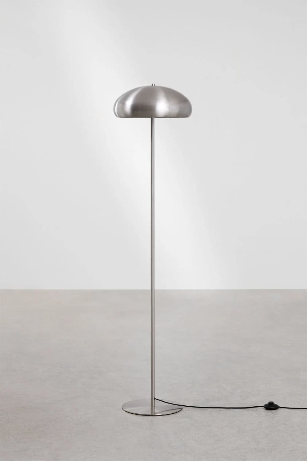 A contemporary floor lamp with a brushed metal finish. It features a circular base, a slender vertical stem, and a mushroom-shaped shade that curves downwards. A black power cord with an inline foot switch is visible extending from the base. — 3D model