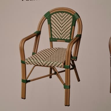A light brown and green wicker armchair with a curved back and armrests. The seat and back are woven in a checkerboard pattern, alternating between light beige and green. The frame appears to be made of bent bamboo or rattan, with green wicker bindings at various joints. The chair has four legs, connected by crossbars for stability. It is designed for outdoor or bistro use. — 3D model