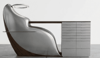 A highly modern and sculptural desk unit featuring an integrated ergonomic chair, a work surface, and a multi-drawer storage cabinet. The design combines a curved, polished metal shell with dark wood accents and a glass side shelf. An illuminated ring fixture is positioned above the chair. — 3D model