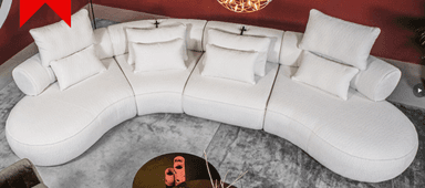 A large, modular, curved sectional sofa with a rounded chaise. The sofa is upholstered in a textured white fabric and features multiple loose back and throw pillows. The design is contemporary and appears to be a low-profile model. — 3D model