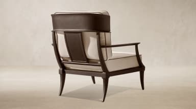 A contemporary lounge armchair featuring a dark-toned exposed metal frame and plush, light-colored upholstered cushions. The chair has a distinctive backrest with a wide, curved top rail and vertical support elements, complemented by straight, padded armrests. The legs are subtly tapered, contributing to a sleek and elegant profile. — 3D model