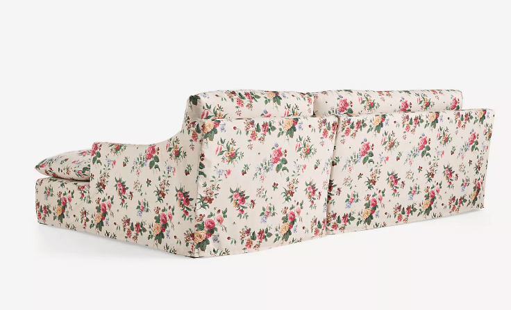 A cream-colored sofa upholstered in a floral fabric with a pattern of roses, peonies, and other flowers in shades of pink, yellow, green, and red. The sofa features a low profile with a slightly sloped armrest. The upholstery covers the entire structure, including the base, cushions, and back. — 3D model