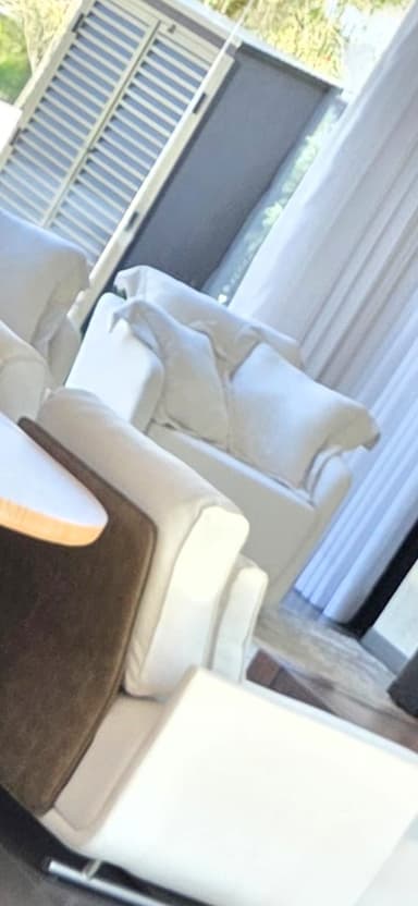 A modern, upholstered armchair in a light, neutral color, featuring soft, rounded lines and plush cushioning. The chair includes a loose back cushion and two decorative throw pillows, suggesting a design focused on comfort and contemporary aesthetics. — 3D model