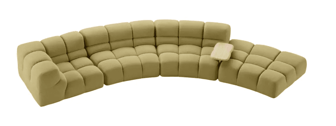 A modular, sectional sofa with a curved configuration. Each module consists of multiple tufted cushions, creating a soft, pillowed appearance. The sofa is upholstered in a textured fabric and features a light-colored, organically shaped tray attachment on one of the sections. — 3D model