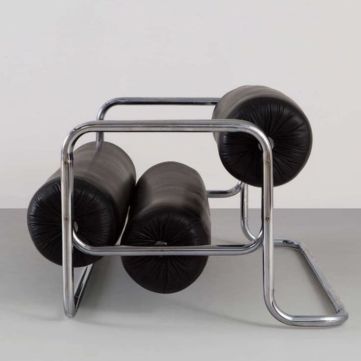 A modern armchair with a tubular chrome frame and three cylindrical black leather cushions. The cushions are tufted and arranged horizontally within the frame, forming the seat and backrest. The frame has a cantilevered base. — 3D model