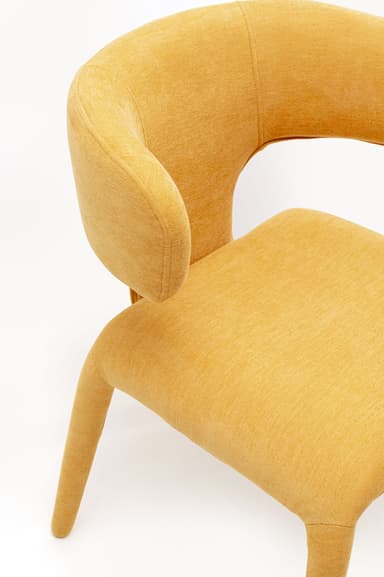 A contemporary armchair with a distinctive curved backrest that flows into integrated armrests. The seat and back are upholstered in a textured, mustard-yellow fabric. It is supported by four tapered legs that extend outwards, also upholstered in the same fabric. The design emphasizes organic curves and a cohesive upholstered form. — 3D model