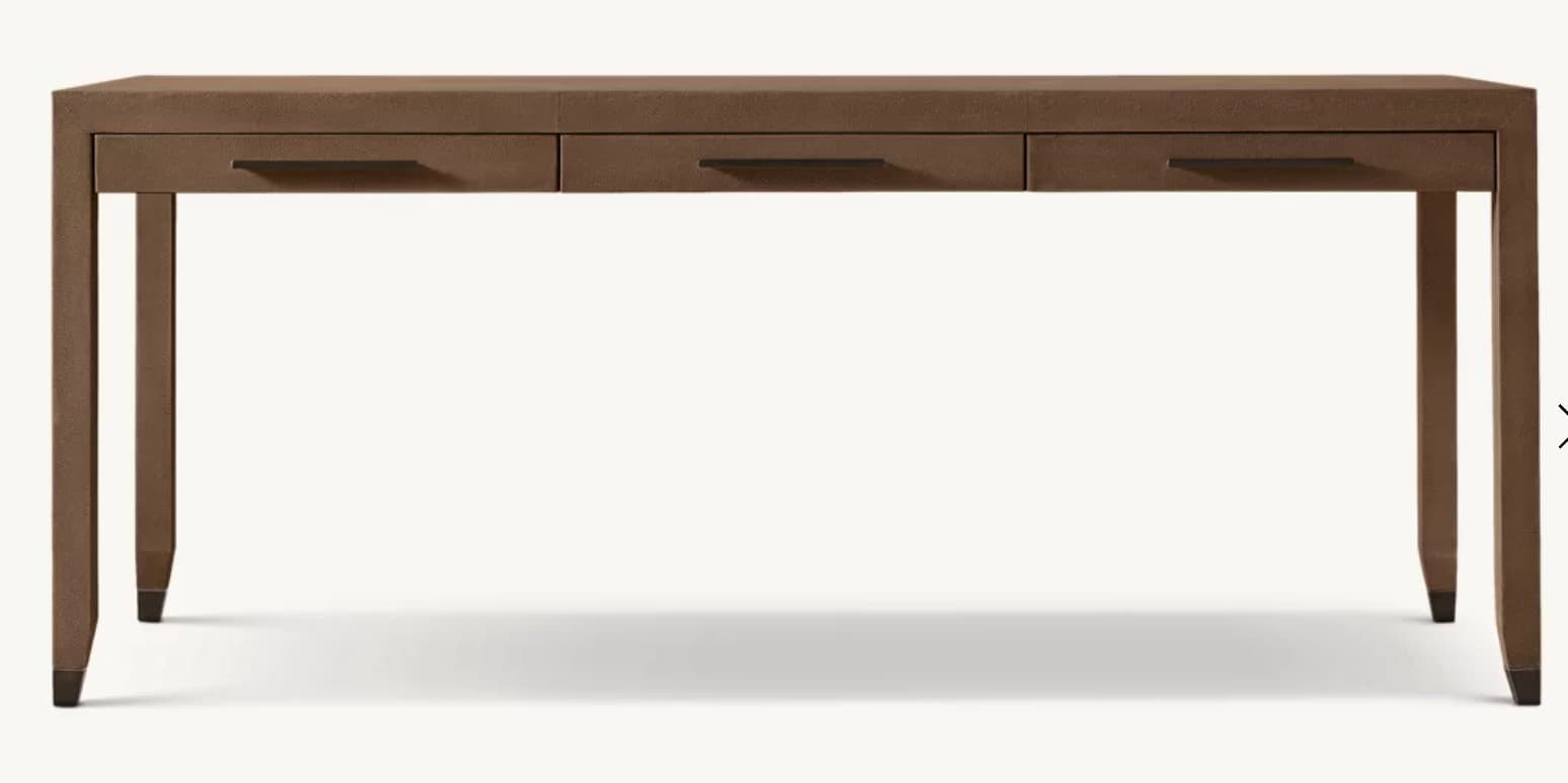 A rectangular console desk featuring three integrated drawers, all encased in a textured brown material, likely leather or faux leather. Each drawer is equipped with a dark, recessed bar handle. The table stands on four straight legs that subtly taper towards the bottom, capped with dark, possibly metallic, feet. The overall design is sleek and minimalist. — 3D model