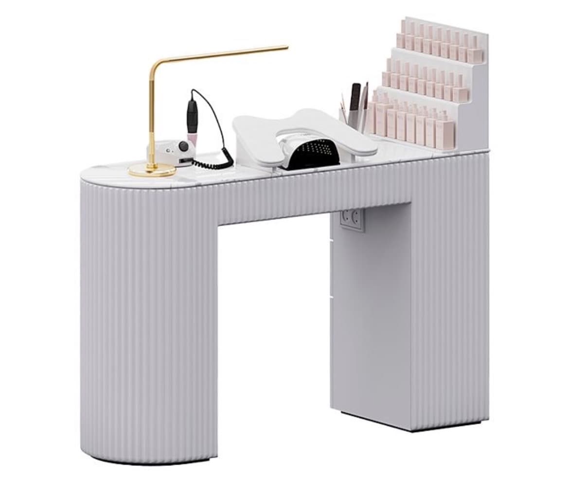 A modern manicure station featuring a white and light grey finish with a faux marble tabletop. The desk is supported by a curved, fluted leg on the left and a rectangular cabinet-style leg on the right, which incorporates an integrated nail polish display rack. It is equipped with a gold-finished task lamp, a nail drill, and a UV curing lamp, making it a complete setup for professional nail services. — 3D model