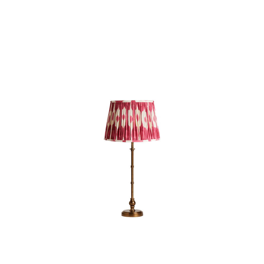 A table lamp with a pleated lampshade featuring a red and off-white ikat-style pattern. The base and stem are made of metal, with a textured finish on the stem and a round, flat base. The lampshade has a straight-sided, slightly flared conical shape. — 3D model
