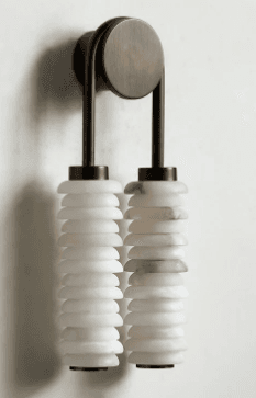 A wall-mounted lamp with a dual cylindrical shade design. The fixture features a brushed metallic finish on its mounting hardware and support arms, with two vertical suspension elements. Each suspension element terminates in a stacked, cylindrical shade crafted from a translucent, possibly alabaster or marble-like material, showing natural striations and variations in color. — 3D model