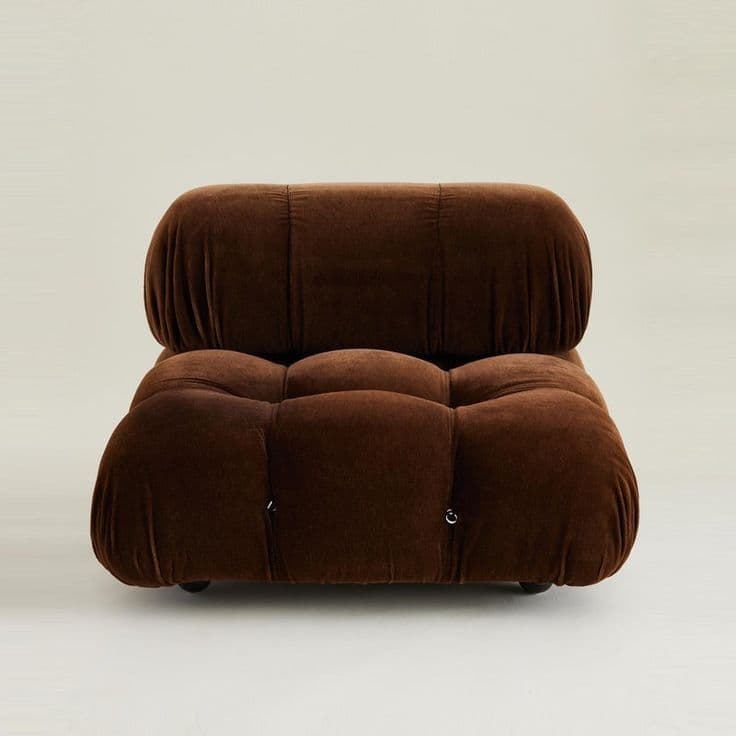 A modular armchair with a plush, tufted design upholstered in a dark brown velvet-like fabric. The armchair features a rounded silhouette, with distinct cushioned sections for the seat and back. The backrest is a single, large padded cushion with vertical channel tufting, while the seat consists of multiple smaller, deep button-tufted cushions arranged in a grid. It appears to be supported by small, discreet wheels or casters, suggesting mobility. The overall aesthetic leans towards a contemporary or retro-modern style. — 3D model