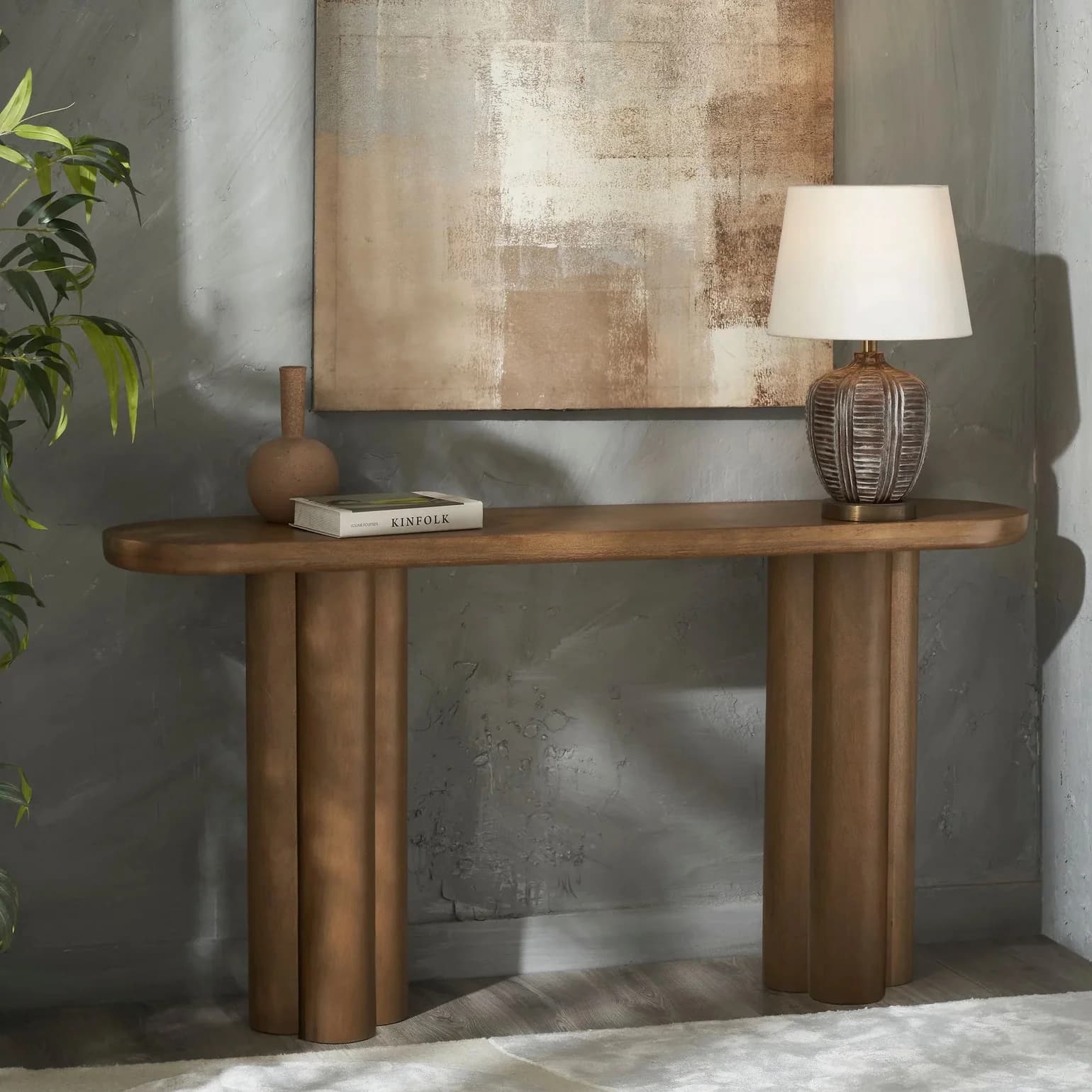 A modern wood console table featuring an elongated, rectangular tabletop with rounded short edges, supported by two sets of three vertically oriented, pill-shaped cylindrical legs. The table has a uniform medium-brown wood finish. — 3D model