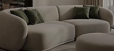 A modern, curved sectional sofa upholstered in a light beige fabric, accompanied by a matching round ottoman. It features soft, rounded lines and includes two dark green throw pillows. — 3D model