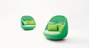 A vibrant green outdoor pod daybed featuring a durable woven synthetic rattan frame, shaped into a semi-enclosed, cocoon-like structure. The interior is fitted with a round base cushion and several throw pillows in varying shades of light green, providing plush comfort. The design suggests a contemporary and relaxed aesthetic, suitable for outdoor lounging. — 3D model