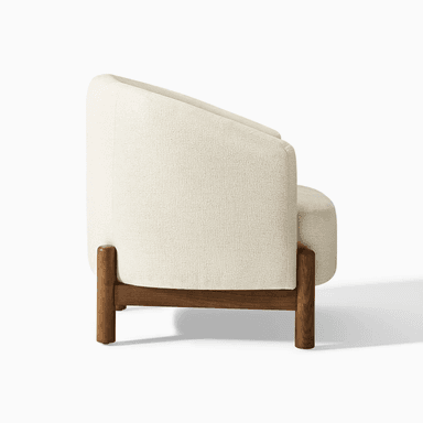 A modern armchair upholstered in a textured, light-colored fabric. It features a gently curved backrest that extends to armrests. The chair is supported by a dark wood frame with distinct legs that are cylindrical at the bottom and square where they meet the seat. — 3D model
