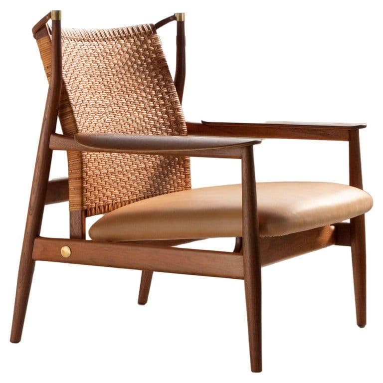 A mid-century modern lounge armchair featuring a dark teak wood frame, a woven cane backrest, and a tan leather seat cushion. The chair has open armrests, cylindrical tapered legs, and brass detailing on the frame. — 3D model