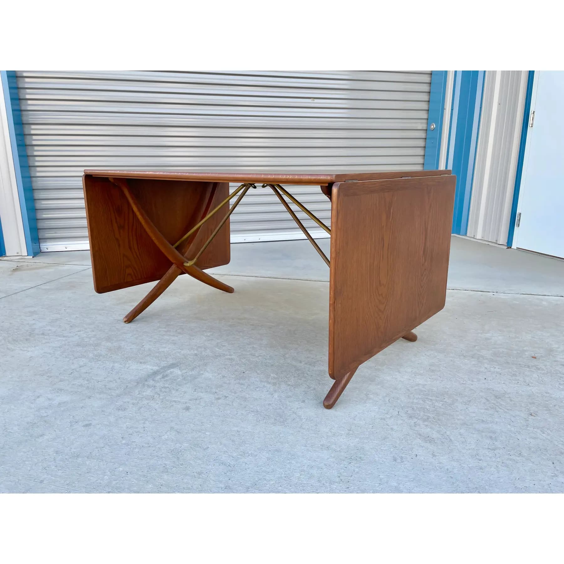 A rectangular Mid-Century Modern drop-leaf gateleg dining table crafted from medium-toned wood, likely teak. The table features two hinged leaves that can be folded down to save space, supported by a gateleg mechanism when extended. The visible wood grain is warm with a semi-gloss finish, and the design is characterized by clean lines and functional versatility typical of the era. — 3D model