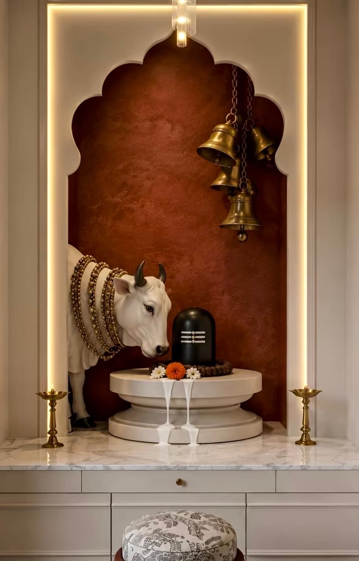 An integrated modern Hindu home temple unit, featuring a multi-tiered design with a marble countertop, storage drawers, and an arched spiritual niche. The niche houses religious artifacts including a Nandi statue and a Shiva Lingam, accented by brass bells and oil lamps. The unit is illuminated with integrated LED lighting along the arch and a delicate pendant light fixture. — 3D model