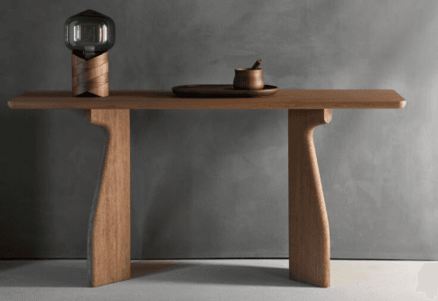 A minimalist wooden bench crafted from light-colored wood, likely oak or ash, featuring a rectangular top with subtly rounded edges. The bench is supported by two distinctively shaped, thick slab legs that are positioned inward from the ends, providing a stable and sculptural base. The overall aesthetic is clean and contemporary. — 3D model