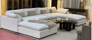 A modular sectional sofa with multiple seating components arranged in a U-shape. It features a low profile, deep seating, and ample cushioning. The sofa is upholstered in a white material and comes with several throw pillows in neutral tones. A beige knitted throw is draped over one of the chaise sections. — 3D model