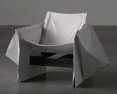 A contemporary lounge chair featuring a dark-stained slatted wooden frame over which a light grey fabric is loosely draped to form the seat, back, and armrests. The design is deconstructed and minimalist. — 3D model