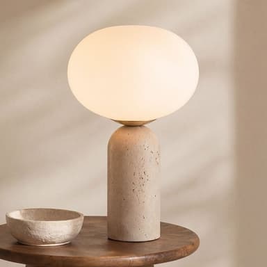 A modern table lamp featuring a cylindrical base made of textured, light-colored travertine, topped with a large spherical opaque white glass diffuser that emits a soft, ambient light. The design is minimalist and sculptural. — 3D model