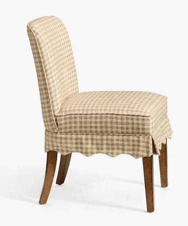 A fully upholstered dining chair featuring a beige and white gingham check pattern. The chair has a tall, slightly curved backrest and a padded seat. A decorative scalloped skirt covers the lower part of the seat frame, partially concealing the upper portion of the four tapered wooden legs. The design suggests a blend of traditional and country-style aesthetics. — 3D model
