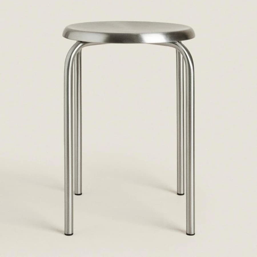 A contemporary stool featuring a circular, brushed metal seat and three cylindrical legs connected by a central support structure. The legs are rounded and extend from beneath the seat. — 3D model
