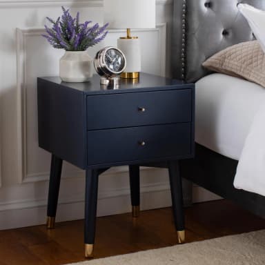 A compact, dark navy blue nightstand featuring two drawers, spherical brass hardware, and four tapered legs with matching brass caps. Its design suggests a contemporary or modern aesthetic, ideal for bedside use or as an accent piece. — 3D model