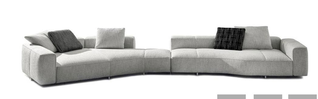 A contemporary modular sectional sofa with a curved design, upholstered in a textured light gray fabric. The sofa features two distinct sections connected to form an 'S' shape. Each section has padded armrests and seat cushions with subtle channel tufting. It is accessorized with three throw pillows: one angled light gray pillow on the left section, and on the right section, a light gray square pillow and a dark gray patterned pillow. — 3D model