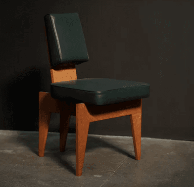 An armless chair featuring a distinctive geometric wooden frame with a light-colored, possibly burled, wood grain. The seat and separate backrest are upholstered in a dark green material, likely leather or a high-quality synthetic, offering a plush appearance. The wooden base is composed of thick, angular planks forming the legs and supporting structure, with a splayed design that tapers slightly towards the floor. The chair has a low profile backrest, suggesting an accent or side chair function. — 3D model