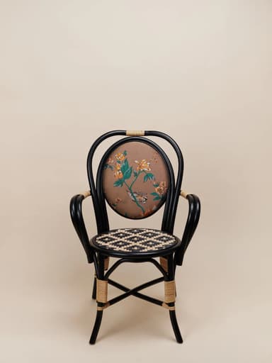 An armchair featuring a black painted rattan or bentwood frame, an oval upholstered backrest with a detailed floral and bird pattern on a brown background, and a woven cane seat with a distinctive black and natural geometric pattern. The chair includes rattan-wrapped accents on the arms and legs, contributing to its eclectic bistro-inspired aesthetic. — 3D model