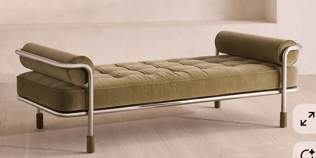 A modern daybed featuring a tufted mattress and cylindrical bolster pillows at either end. The frame is constructed from polished chrome tubing, with the legs having dark wood accents at the bottom. The upholstery appears to be a plush velvet or similar fabric. — 3D model