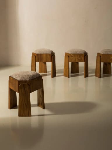 A wooden stool with an upholstered hexagonal seat. The stool has four legs, with two facing front and two facing back, joined by a central structural element. The wooden frame exhibits a grain pattern characteristic of natural wood. — 3D model