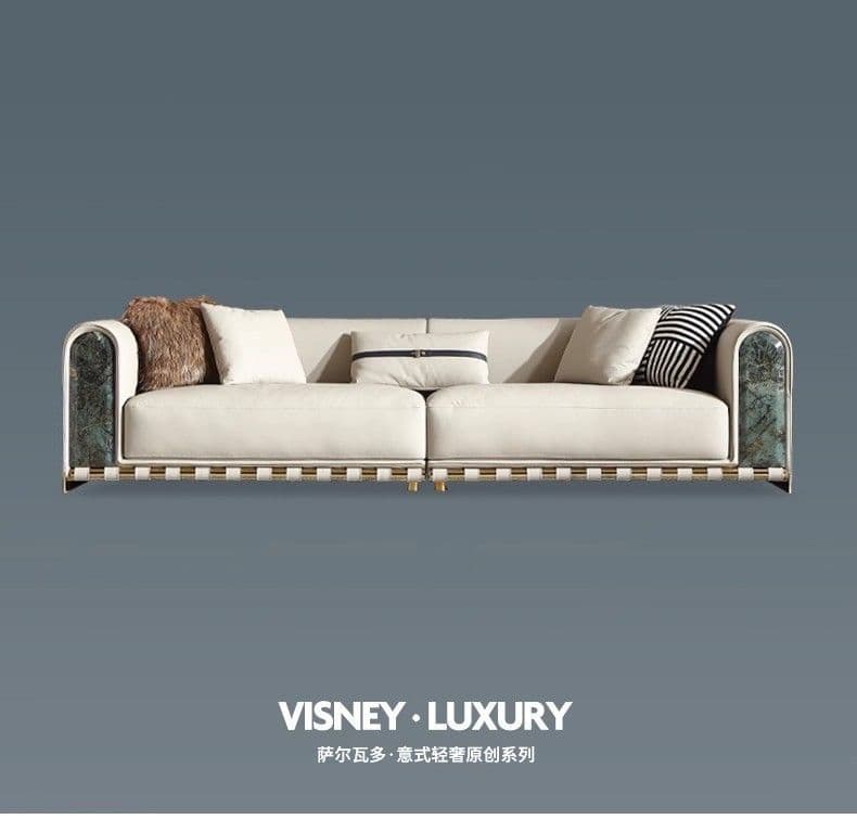 A luxurious modern sofa featuring a cream-colored upholstered body, curved green marble armrests with brass accents, and a distinctive open base composed of brass cylinders integrated with light-colored straps. Several decorative pillows are arranged on the sofa. — 3D model