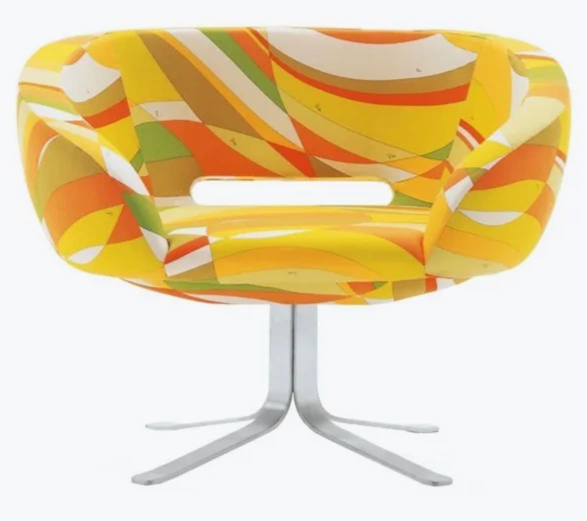 A modern accent chair with a rounded, low-profile backrest and seat. The upholstery features a vibrant, abstract geometric pattern in shades of yellow, orange, green, and white. It has an integrated armrest design and a central opening in the seat. The chair is supported by a brushed metal pedestal base with four splayed legs. — 3D model