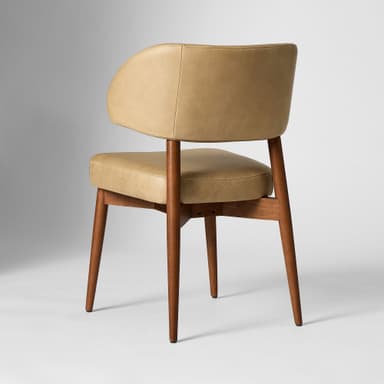 A tan upholstered accent chair with a curved backrest and a cushioned seat. The chair features a wooden frame with four tapered legs. The upholstery appears to be leather or a leather-like material, with visible stitching details on the backrest and seat cushion. The wooden legs and frame have a medium-toned finish. — 3D model