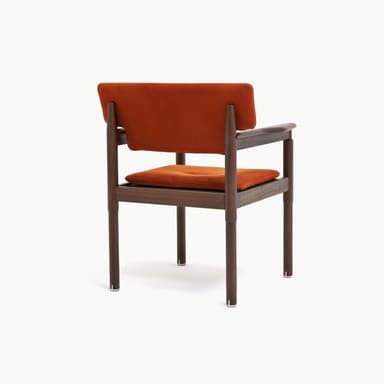 A contemporary armchair featuring a dark wood frame and rust-colored upholstered seat and backrest. The backrest is rectangular with cut-outs to accommodate the rounded wooden armrests, which extend from the rear support posts. The legs are cylindrical and straight, connected by stretcher bars beneath the seat. The seat cushion is subtly tufted. — 3D model