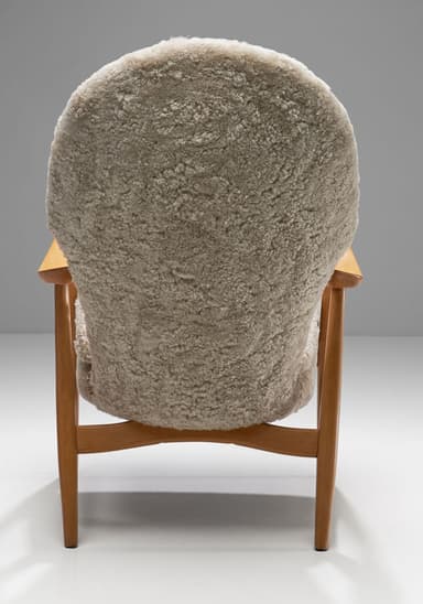 A high-backed armchair with a wooden frame and plush sheepskin upholstery. The frame consists of curved wooden arms and legs. The seat and back are fully upholstered in a textured, cream-colored sheepskin material, giving it a soft and inviting appearance. The design suggests a focus on comfort and organic forms. — 3D model