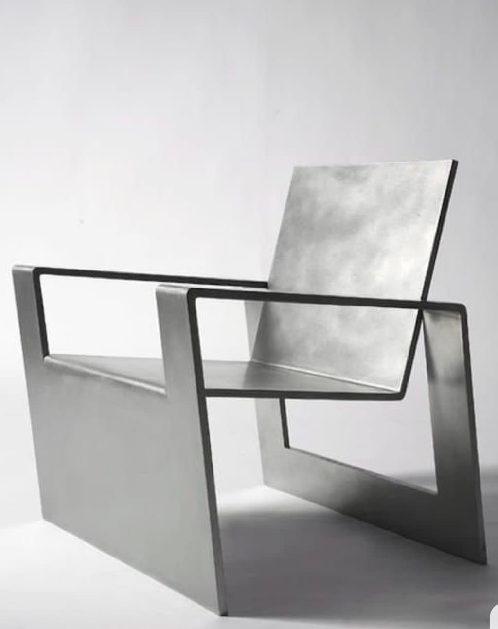 A modern armchair with a minimalist design, constructed from flat metallic planes. It features a low backrest, a seat, and armrests that are integrated into the main structure. The base is formed by angled supports that create a geometric silhouette. The overall aesthetic is industrial and sleek. — 3D model